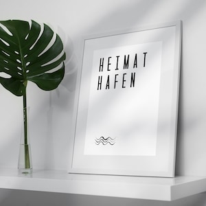 K&ouml;nnte beinhalten: Ein wei&szlig;er gerahmter Druck mit dem Text "HEIMAT  HAFEN" und einem Wellenlinien-Design. Der Druck befindet sich auf einem wei&szlig;en Regal mit einer gr&uuml;nen Pflanze in einer durchsichtigen Glasvase.