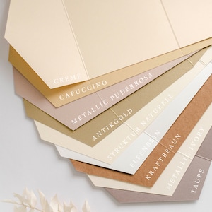 Op de afbeelding: Een verzameling papierstalen in verschillende tinten beige, bruin en roze. De papierstalen zijn gelabeld met namen zoals "Creme", "Cappuccino", "Metallic Puderrosa", "Antikgold", "Struktur Naturell", "Elfenbeen", "Kraftbraun", "Metallic Ivory" en "Taupe".