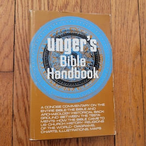 Op de afbeelding: Een vintage "Unger's Bible Handbook" boek met een gouden omslag en blauw cirkelvormig ontwerp. De titel van het boek staat in witte en zwarte tekst. De omslag bevat ook tekst die de inhoud van het boek beschrijft.