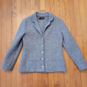 Op de afbeelding: Een grijze wollen blazer met een reverskraag, twee voorzakken en een sluiting met vier knopen. De blazer heeft een getailleerde pasvorm en is gemaakt van een zachte, getextureerde stof. Het label luidt "Country Set".