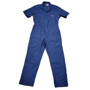 May include: A solid blue short-sleeve coverall featuring a collared neckline, a front button-up closure, and two chest pockets. A small red and white Dickies brand label is stitched onto the left chest pocket area of this one-piece garment.