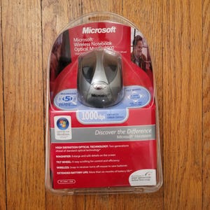 May include: A Microsoft Wireless Notebook Optical Mouse 4000 in its original clear plastic blister packaging. The mouse is silver and black with the Microsoft logo. The packaging features red and white text, including 1000 dpi and Windows Vista.