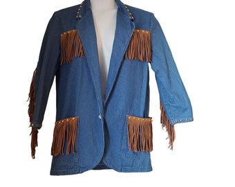 May include: A blue denim blazer with brown fringe accents on the pockets, sleeves, and chest. The blazer has gold-colored stud details along the collar and pockets. A single button closure is visible.