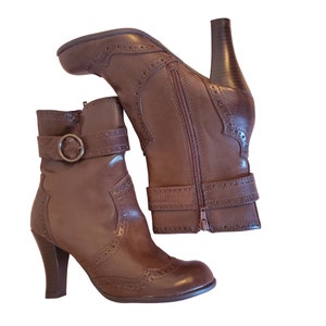May include: A pair of brown leather ankle boots with a buckle detail and a pointed toe. The boots have a high heel and a zip on the inside of the ankle.