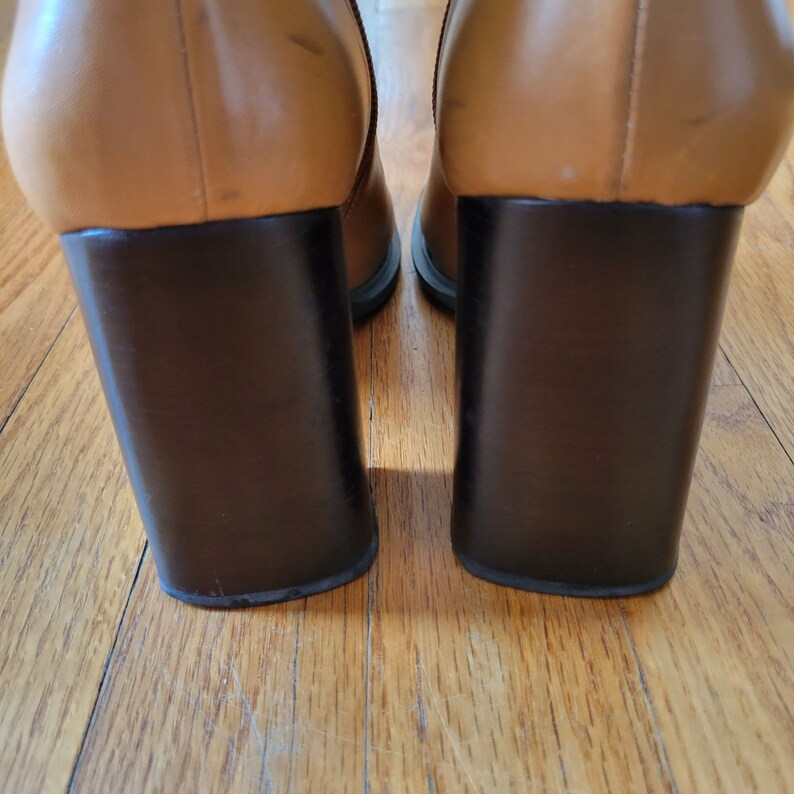 May include: A pair of brown leather heeled boots with a dark brown block heel.