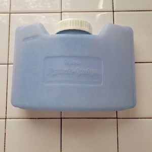 Puede incluir: Una cantimplora Igloo Playmate de color azul claro. La cantimplora rectangular tiene una tapa de rosca blanca y una superficie texturizada. El logotipo de Igloo y la información del producto están impresos en la parte delantera.