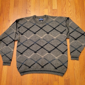 May include: A gray sweater with a black and blue diamond pattern. The sweater has a crew neck and long sleeves. The brand name "Jantzen" is visible on the tag.