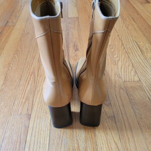 May include: A pair of tan leather ankle boots with black heels. The boots have a zipper on the inside of each boot.