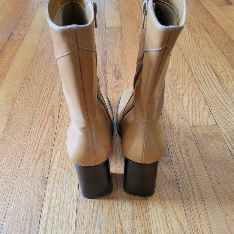 May include: A pair of tan leather ankle boots with black heels. The boots have a zipper on the inside of each boot.
