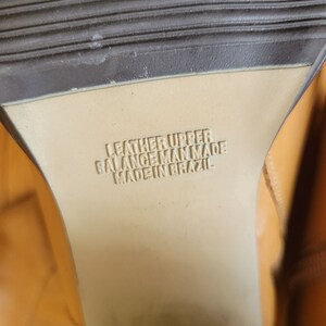 May include: Close-up of the bottom of a brown leather shoe with the text "Leather Upper Balance Man Made Made in Brazil" printed on the sole.