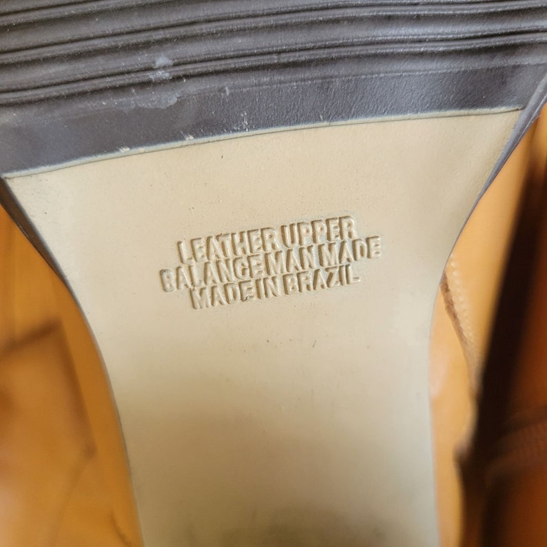 May include: Close-up of the bottom of a brown leather shoe with the text "Leather Upper Balance Man Made Made in Brazil" printed on the sole.