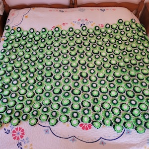 May include: A green and white crocheted blanket with a floral pattern. The blanket is made up of many small, round flowers.