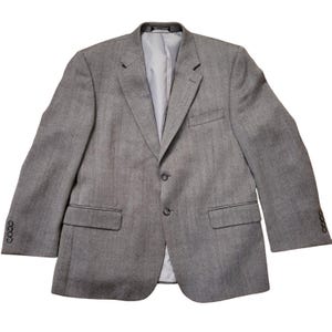 May include: A gray blazer with a two-button closure, two front pockets, and four buttons on each sleeve cuff. The blazer has a notched lapel and a light gray lining. The fabric has a subtle herringbone pattern.