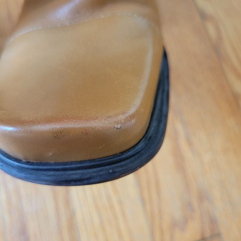 May include: Close-up of the bottom of a brown leather boot with a black rubber sole.