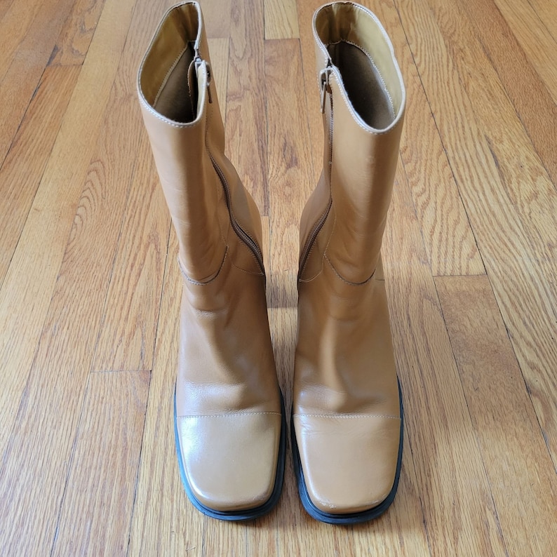 May include: A pair of brown leather boots with a square toe and a zipper on the side.