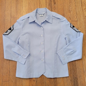 Peut inclure: Chemise boutonnée bleu clair à manches longues et col. La chemise présente des rayures noires et blanches sur les manches. La chemise a une coupe ajustée et est boutonnée. La chemise est en tissu de couleur claire.