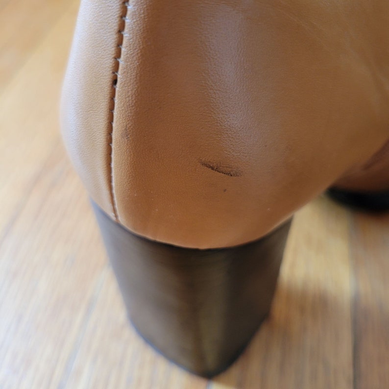 May include: Tan leather heeled boots with a black heel. The boots have a slight scuff mark on the back.