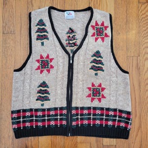 May include: Tan knitted vest with a black trim and zipper. The vest features Christmas tree and star designs in green and red, with a plaid pattern at the bottom. A cozy, festive garment.