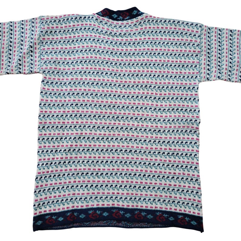 Op de afbeelding: Een vintage gebreide trui met een herhalend patroon van kleine rode, teal en marineblauwe vormen op een cr&egrave;mekleurige achtergrond. De trui heeft een marineblauwe kraag en zoom met een decoratief patroon. De mouwen zijn kort en de algehele stijl is casual.