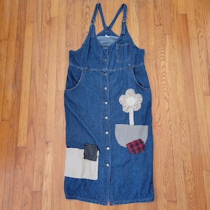 Puede incluir: Vestido de peto de mezclilla azul con tirantes ajustables y cierre de botones. Cuenta con una gran aplicación floral y bolsillos de patchwork con detalles de tela a cuadros y lisa. Una prenda informal de inspiración vintage.
