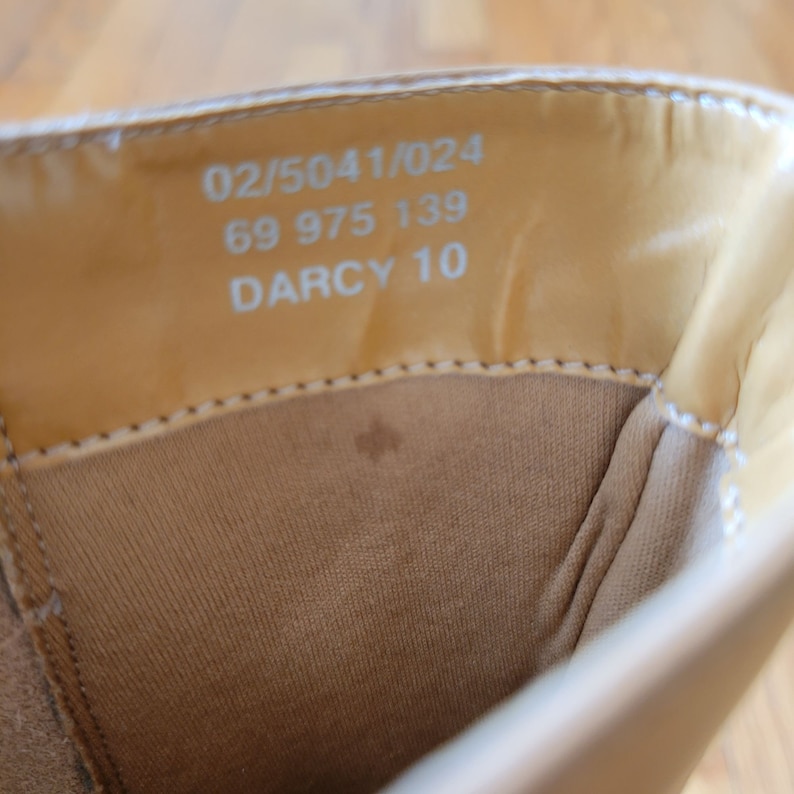 May include: Close-up of the inside of a light brown shoe with the text "02/5041/024 69 975 139 DARCY 10" printed on the insole.