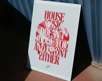 Puede incluir: Un póster blanco con texto rojo que dice "HOUSE MUSIC DOESN'T JUDGE YOU AND I WON'T EITHER". El póster tiene un diseño circular rojo y blanco. El póster está apoyado contra una pared azul.