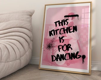 May include: A pink and white framed print with the text "This kitchen is for dancing" in black paint. The print features a vintage image of a woman in a kitchen.