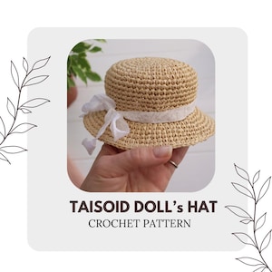 May include: A crocheted doll hat in a light brown color with a white ribbon around the crown. The hat is held in a hand. The text "TAISOID DOLL'S HAT CROCHET PATTERN" is below the hat.