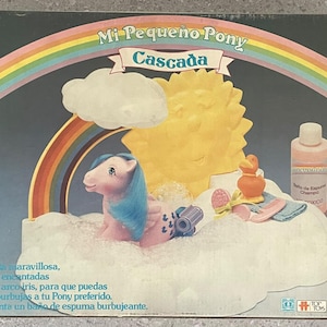 Puede incluir: Una caja de juego Mi Pequeño Pony Cascada que incluye un poni rosa con crin azul, un sol amarillo, una base de nube blanca, un arcoíris, un patito naranja, una botella rosa de baño de espuma y varios accesorios de aseo para el poni.