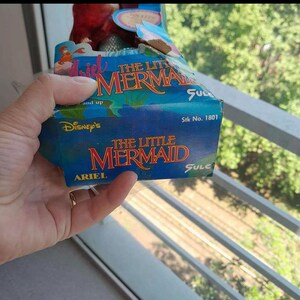 May include: A blue and white box with the text "Disney's The Little Mermaid" and "Ariel" on it. The box has a picture of Ariel, a mermaid, on it. The box is for a toy.