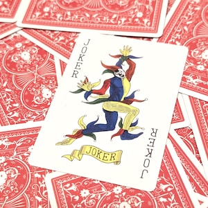May include: A playing card featuring a colorful joker character with the word "JOKER" on the card. The card is set against a background of red playing cards with a floral design.