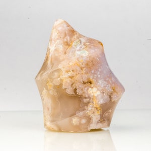 May include: A polished, freeform gemstone with a light brown base colour and intricate patterns of white and yellow. The stone has a smooth, glossy surface and a unique, organic shape, ideal for display or collection.