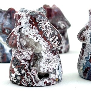 May include: Close-up of several mushroom-shaped stone carvings. The carvings are primarily red, white, and black, with intricate patterns and textures. The mushroom caps have a rounded shape, and the stems are short and stout. The background is white.