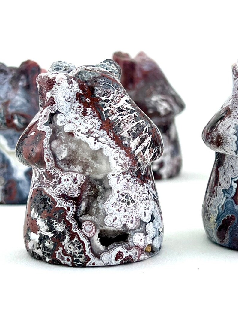 May include: Close-up of several mushroom-shaped stone carvings. The carvings are primarily red, white, and black, with intricate patterns and textures. The mushroom caps have a rounded shape, and the stems are short and stout. The background is white.