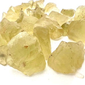 Può includere: Una collezione di pietre grezze giallo limone traslucide con forme irregolari, frastagliate e bordi taglienti. Le pietre presentano una consistenza vetrosa con vari gradi di chiarezza e piccole inclusioni scure sparse sulle superfici.