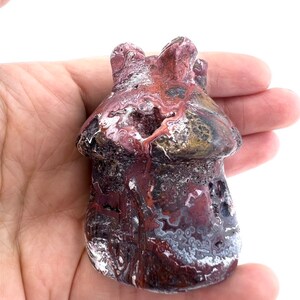 May include: A mushroom-shaped stone sculpture with a textured surface. The sculpture features a mix of burgundy, white, and gray colors. The mushroom has a rounded cap and a textured stem, showcasing natural patterns and variations.