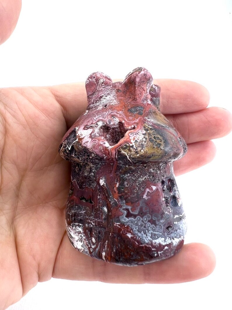 May include: A mushroom-shaped stone sculpture with a textured surface. The sculpture features a mix of burgundy, white, and gray colors. The mushroom has a rounded cap and a textured stem, showcasing natural patterns and variations.