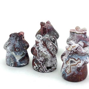 May include: A collection of five mushroom-shaped stone carvings. The carvings feature a mix of colors, including red, gray, white, and brown. The mushroom caps have a textured appearance, and the stems are smooth. The carvings are displayed on a white background.