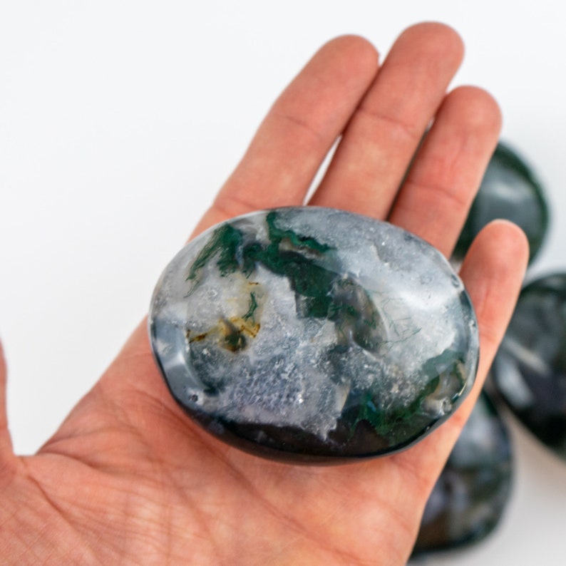 Pu&ograve; includere: Una pietra di agata muschiata lucida, di forma ovale, che mostra motivi grigi, bianchi e verdi. La pietra &egrave; tenuta in mano, con altre pietre simili visibili sullo sfondo. Questa pietra naturale &egrave; adatta per la meditazione o l'esposizione. Misura circa 5 cm di lunghezza.