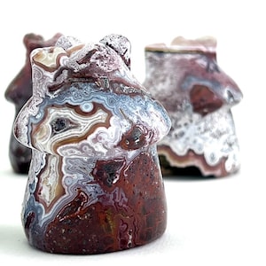 May include: Three mushroom-shaped stone carvings. The front mushroom is in sharp focus, showcasing a detailed pattern of brown, white, and blue swirls. The other two mushrooms are slightly out of focus, with similar color variations.