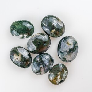 Pu&ograve; includere: Sette pietre di agata muschiata ovali e lucide. Le pietre presentano motivi verde scuro, bianchi e trasparenti. Sono disposte su sfondo bianco, ognuna con un motivo unico. Le pietre misurano circa 3-4 cm di lunghezza.