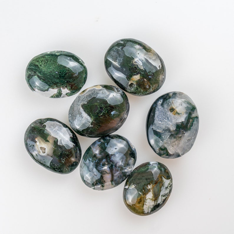 Pu&ograve; includere: Sette pietre di agata muschiata ovali e lucide. Le pietre presentano motivi verde scuro, bianchi e trasparenti. Sono disposte su sfondo bianco, ognuna con un motivo unico. Le pietre misurano circa 3-4 cm di lunghezza.