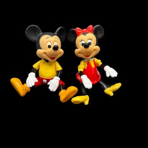 Pode incluir: Duas figuras de Mickey e Minnie Mouse. Mickey est&aacute; vestindo uma camisa amarela, shorts vermelhos e sapatos amarelos. Minnie est&aacute; vestindo um vestido vermelho com um top amarelo, um la&ccedil;o vermelho e sapatos amarelos. Ambos t&ecirc;m orelhas pretas e luvas brancas.