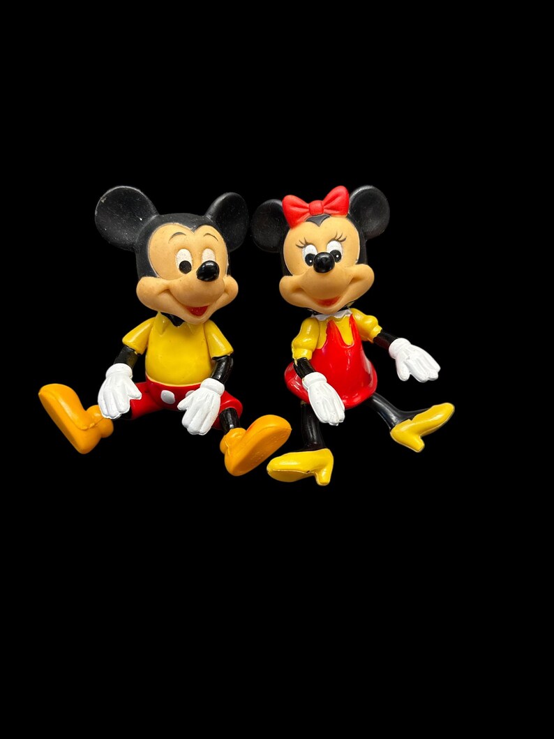 Pode incluir: Duas figuras de Mickey e Minnie Mouse. Mickey est&aacute; vestindo uma camisa amarela, shorts vermelhos e sapatos amarelos. Minnie est&aacute; vestindo um vestido vermelho com um top amarelo, um la&ccedil;o vermelho e sapatos amarelos. Ambos t&ecirc;m orelhas pretas e luvas brancas.