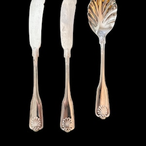 May include: Three silver utensils with ornate shell-shaped handles. Two are butter knives and one is a sugar spoon.