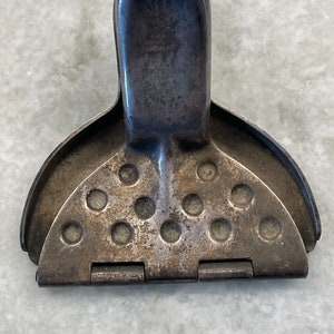 May include: A silver-colored metal citrus juicer with a hinged design and a handle. The juicer has a series of holes for extracting juice from citrus fruits.