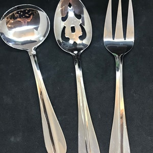 May include: A set of three silver utensils, including a slotted spoon, a serving spoon, and a fork. The utensils have a polished finish and are designed for serving food.