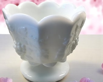 May include: White milk glass bowl with a scalloped rim and a pedestal base. The bowl has a grapevine design.