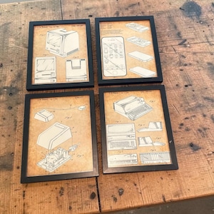 May include: Four framed prints featuring vintage technology blueprints. Each black-framed print showcases detailed line drawings of early computers, phones, and related devices. The prints are displayed on a rustic wooden surface.
