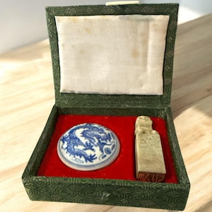 May include: A green box with a red interior contains a blue and white porcelain inkwell with a dragon design and a jade-colored stamp.